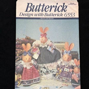 May include: A Butterick 6553 sewing pattern envelope titled Luv 'n Stuff featuring illustrations of four anthropomorphic rabbit dolls wearing lace-trimmed dresses and bonnets. The package displays the brand name, pattern number, and text in English and French.