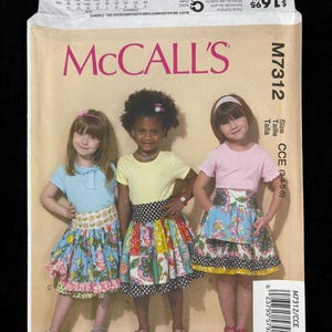 May include: McCall's M7312 sewing pattern for children's skirts. The pattern envelope features three young girls modeling the finished skirts. The skirts have a tiered design with floral and patterned fabrics. The envelope includes size options.