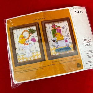 May include: A cross-stitch kit titled "Bath Time" featuring two framed designs. One shows a yellow duckling at a sink, the other in a bathtub. The kit includes printed designs, wool yarn, and cotton embroidery floss.