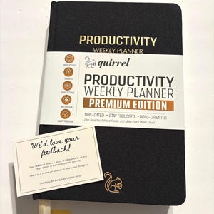 May include: A black Productivity Weekly Planner with the text "Productivity Weekly Planner Premium Edition" and "quirrel" logo. Includes a small card that says "We'd love your feedback!" and a ribbon bookmark.