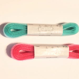 May include: Two rolls of hook and loop tape, one turquoise and one pink. The tape is packaged on white cardboard with the brand name "Sew-ology" printed on it. The price is $1.99 per roll.