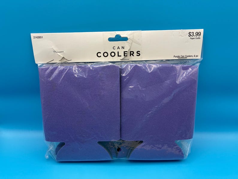 May include: A package of six purple can coolers. The coolers are made of a foam-like material and are packaged in a clear plastic bag. The package has a white header with the words "CAN COOLERS" printed in black.