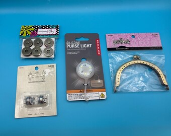 May include: A collection of sewing and craft supplies including a pack of six antique magnetic snaps, a pack of two magnetic snaps measuring 1/2 inch, a silicone purse light with two light settings, and a brass-toned metal purse frame.