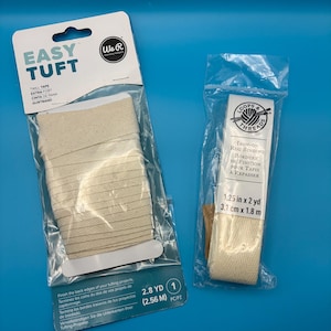 May include: Two packages of craft supplies on a blue background. One package contains beige twill tape labeled "EASY TUFT" and the other contains iron-on rug binding. The "EASY TUFT" package contains 2.8 yards (2.56 m) of tape.