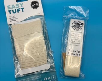 May include: Two packages of off-white twill tape and rug binding. The left package is labeled Easy Tuft and contains 2.8 yards of tape. The right package is labeled Loops & Threads Iron-on Rug Binding, measuring 1.25 inches by 2 yards.