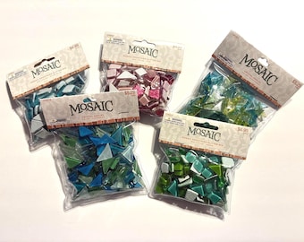May include: Five clear plastic bags containing assorted mosaic tiles in various shapes and colors, including blue, pink, green, and teal. Each bag features a header card with the brand name Mosaic and text identifying the specific tile mix.