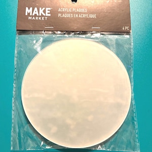 May include: A package of four acrylic plaques from the Make Market brand. The plaques are round and white, and are packaged in a clear plastic bag. The packaging also includes the text "Acrylic Plaques" and "Plaques en Acrylique".