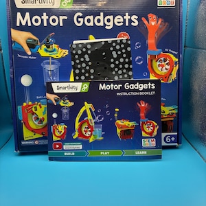 May include: A blue box set of Smartivity Motor Gadgets, a STEM educational building activity for ages 6+. The box features images of the included gadgets, including a tornado maker and air puppet. An instruction booklet is in front.