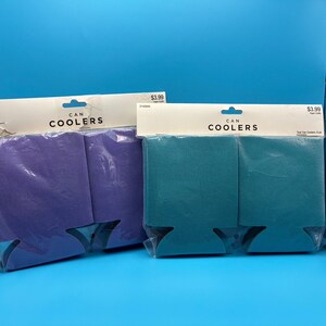 May include: Two can coolers, one purple and one teal, are displayed in their original packaging. The packaging includes the text "CAN COOLERS". The coolers are designed to keep beverages cold.