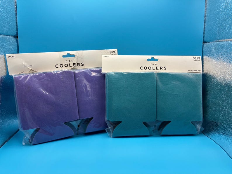 May include: Two can coolers, one purple and one teal, are displayed in their original packaging. The packaging includes the text "CAN COOLERS". The coolers are designed to keep beverages cold.