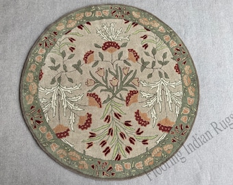 May include: Round rug with a floral design. The rug features a central pattern of stylized flowers and leaves in shades of peach, green, and white against a beige background. A green border with floral accents surrounds the central design. The rug is circular.