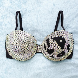 May include: A black bra with iridescent rhinestones covering the entire surface. The rhinestones are arranged in a pattern that resembles a swirl or a wave.