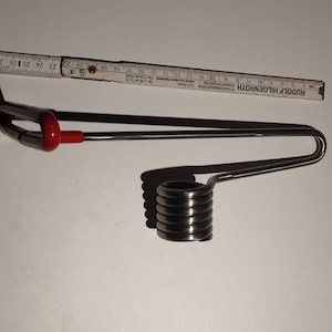 May include: A metal tool with a red handle and a coiled end, possibly for mechanical use. A wooden ruler with black markings is also present, showing measurements in centimetres.