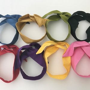 May include: Eight fabric headbands in various colours, including blue, yellow, green, black, red, purple, and pink. The headbands are tied in a knot at the top.