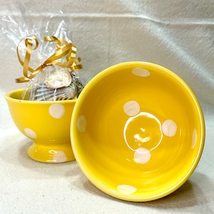 May include: Two yellow ceramic bowls with white polka dots. The bowls are empty and sitting on a white surface.