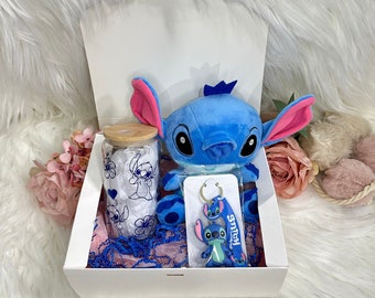 May include: A white gift box filled with blue and pink tissue paper. The box contains a blue Stitch plush toy, a clear glass jar with a blue and white Stitch design, and a blue Stitch keyring.