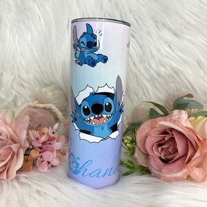 May include: A blue and white stainless steel tumbler featuring a cartoon image of Stitch from Lilo & Stitch. The tumbler has a blue ombre design and the word "ohana" written on the bottom.