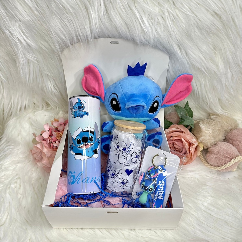 May include: A gift box filled with Stitch themed items. The box contains a blue plush Stitch toy, a blue and white tumbler with Stitch images, a glass jar with a blue and white Stitch design, and a blue Stitch keychain with the text "Stitch happily ever after".