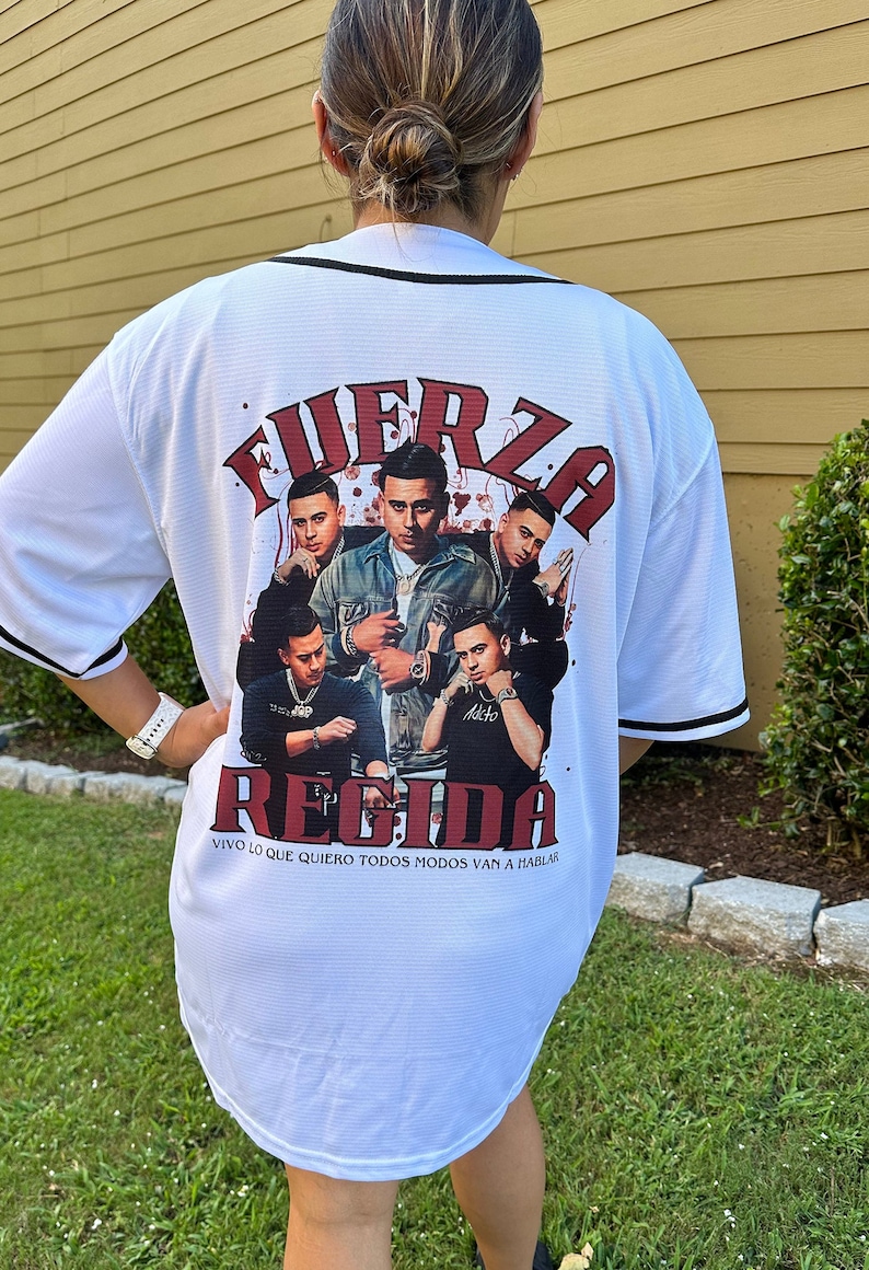 Puede incluir: Jersey de b&eacute;isbol blanco con un estampado gr&aacute;fico rojo y negro de un grupo de hombres con el texto "FUERZA REGIDA" y "VIVO LO QUE QUIERO TODOS MODOS VAN A HABLAR" en la espalda.