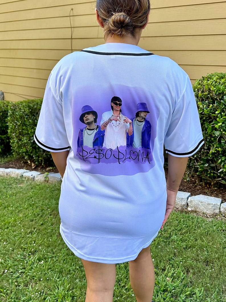 May include: White baseball jersey with a purple and white graphic print of three people wearing hats and the text "$2SO PLOMA".