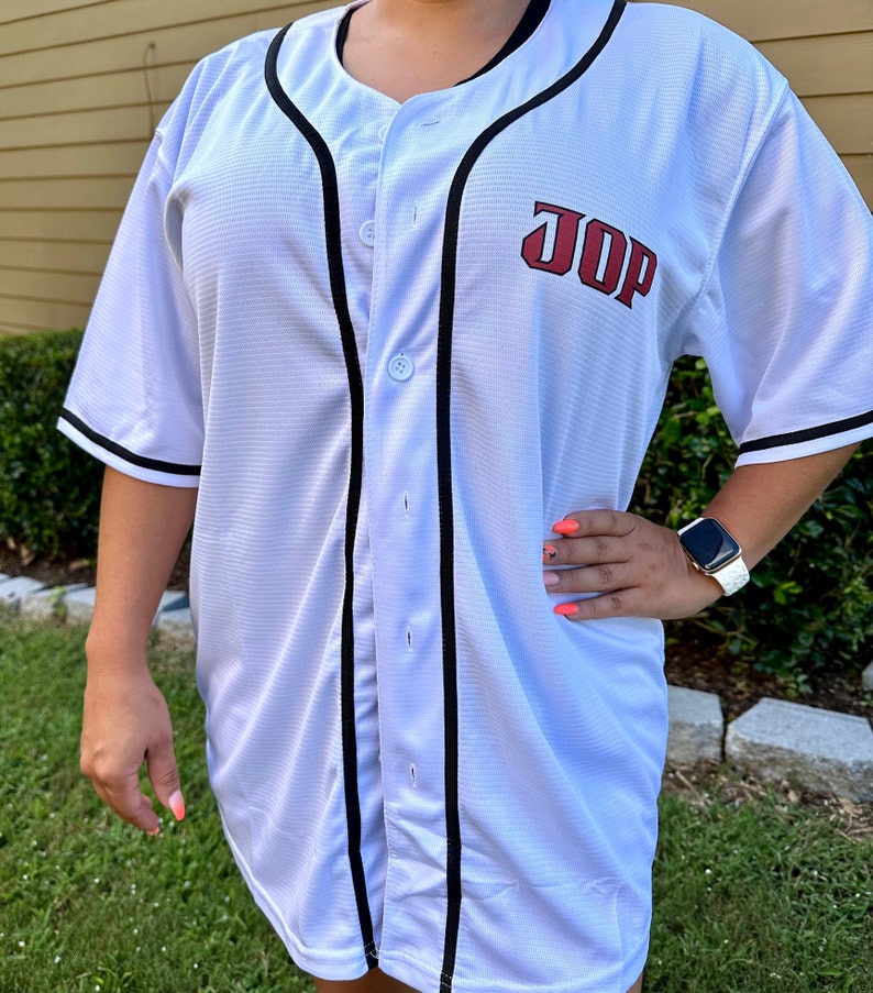 Puede incluir: Jersey de b&eacute;isbol blanco con ribetes negros y letras rojas que dicen "JOP".