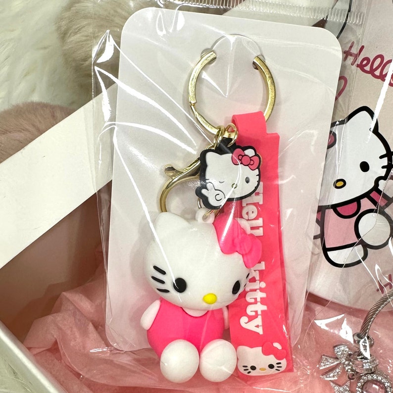 Puede incluir: Llavero Hello Kitty rosa con un anillo de llave dorado y un dije Hello Kitty rosa. El dije tiene una cara blanca con ojos negros y un lazo rosa. El llavero est&aacute; unido a un dije Hello Kitty rosa con el texto "Hello Kitty" en &eacute;l.