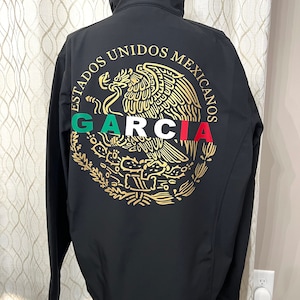 Op de afbeelding: Zwarte softshelljas met een geborduurd Mexicaans wapenschild in goud met een adelaar en de tekst "ESTADOS UNIDOS MEXICANOS GARCIA".