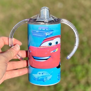 May include: A blue and red stainless steel tumbler with a clear lid and two handles. The tumbler features a cartoon image of Lightning McQueen from the Disney Pixar movie Cars.