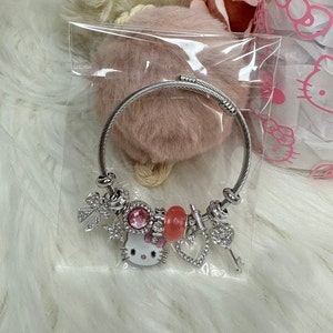Puede incluir: Un brazalete de plata con un dije de Hello Kitty, dijes de cristal rosa y transparente, y un dije de llave.