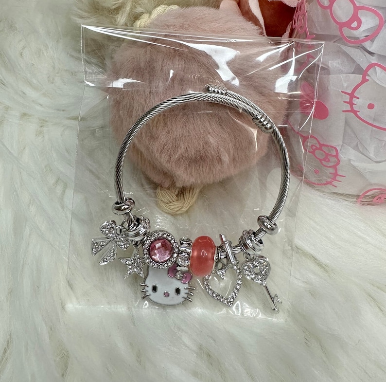 Puede incluir: Un brazalete de plata con un dije de Hello Kitty, dijes de cristal rosa y transparente, y un dije de llave.