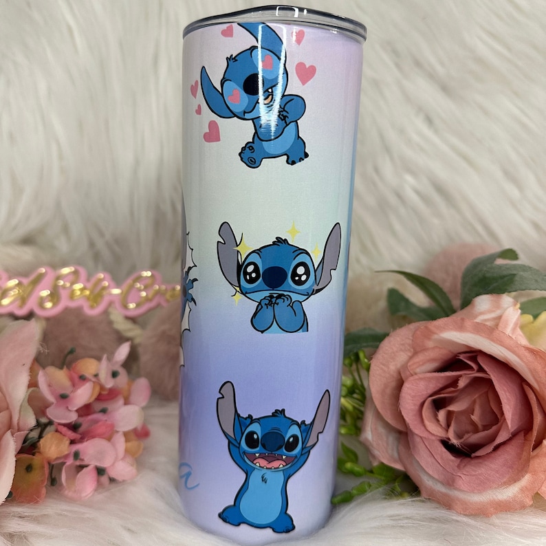 Puede incluir: Un vaso de acero inoxidable azul y blanco con un dise&ntilde;o degradado que presenta varias im&aacute;genes de Stitch de Lilo & Stitch. El vaso tiene una tapa transparente.