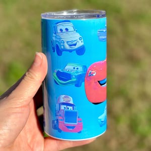 May include: A blue and white tumbler with a Cars theme. The tumbler features images of Lightning McQueen, Mater, and other characters from the movie.