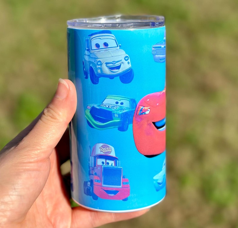 May include: A blue and white tumbler with a Cars theme. The tumbler features images of Lightning McQueen, Mater, and other characters from the movie.
