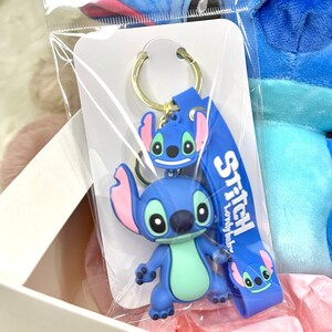 May include: Blue Stitch keyring with a blue and pink Stitch character and a blue strap with the text "Stitch Lovely Stitch".