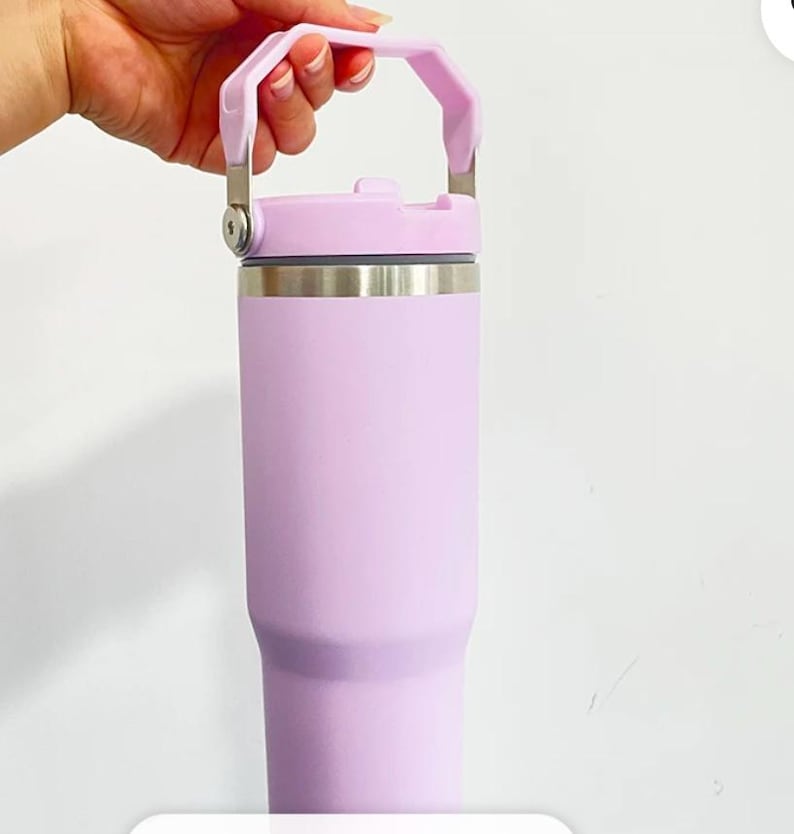 May include: A light purple insulated tumbler with a handle. The tumbler has a stainless steel band near the top and a matching light purple lid. The handle is also light purple and attached to the lid with silver metal hinges.