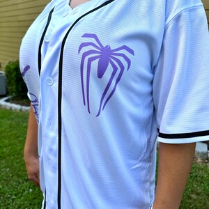 May include: White baseball jersey with black trim and a purple spider graphic on the front.