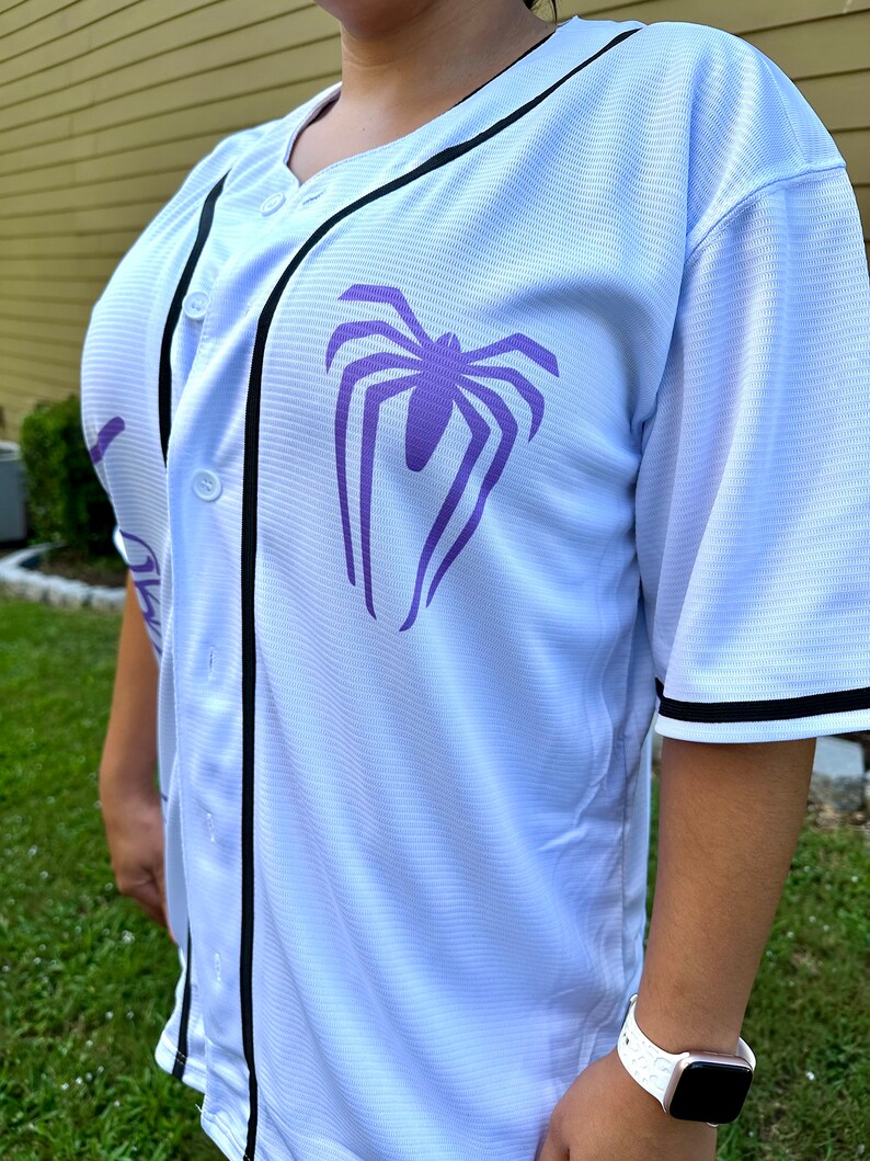 May include: White baseball jersey with black trim and a purple spider graphic on the front.