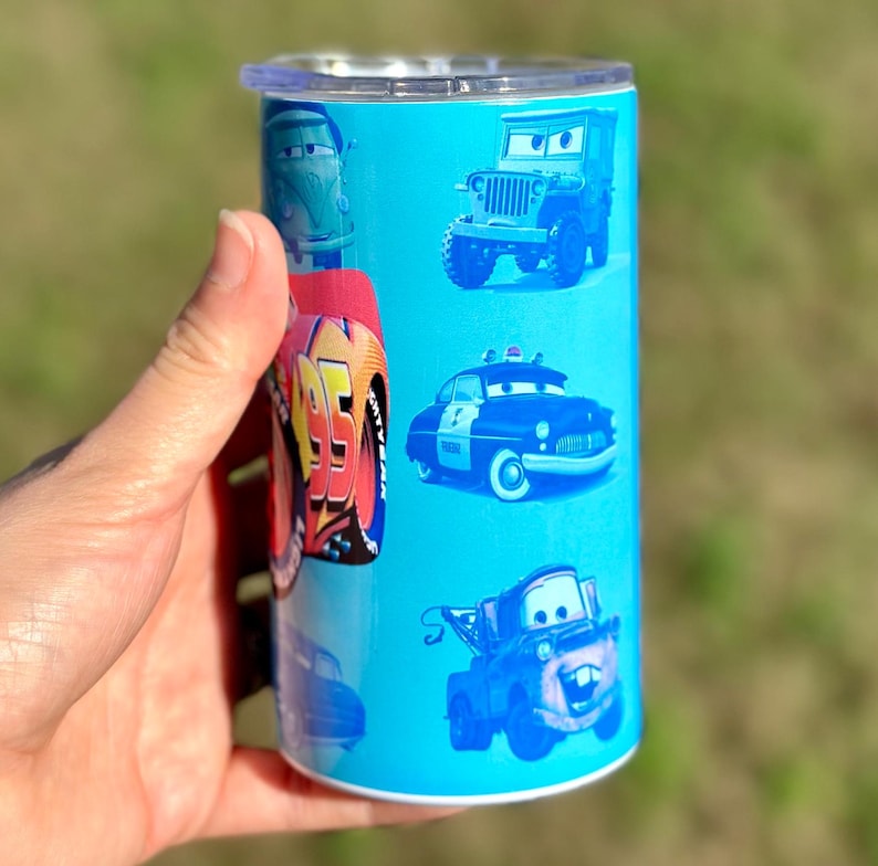 May include: A blue and white tumbler with a Cars theme. The tumbler features images of Lightning McQueen, Mater, and other characters from the movie.