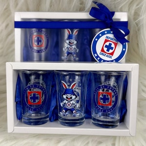 May include: A set of six shot glasses in a white box with a blue ribbon. The glasses feature a blue and white logo with a cartoon bunny and the text "Club de Futbol Cruz Azul".