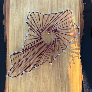 May include: A wooden board with a red string art design in the shape of a state. The string is wrapped around silver tacks.