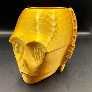 Może przedstawiać: Złota doniczka 3D wydrukowana w kształcie głowy C-3PO z Gwiezdnych Wojen. Doniczka ma fakturowaną powierzchnię i szczegółowy projekt.