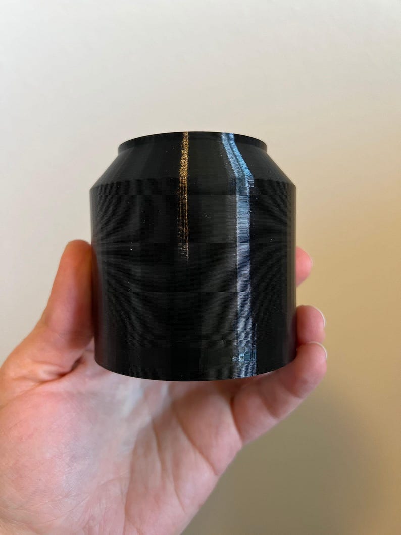 Puede incluir: Un recipiente cil&iacute;ndrico negro impreso en 3D con una superficie lisa y ligeramente texturizada.