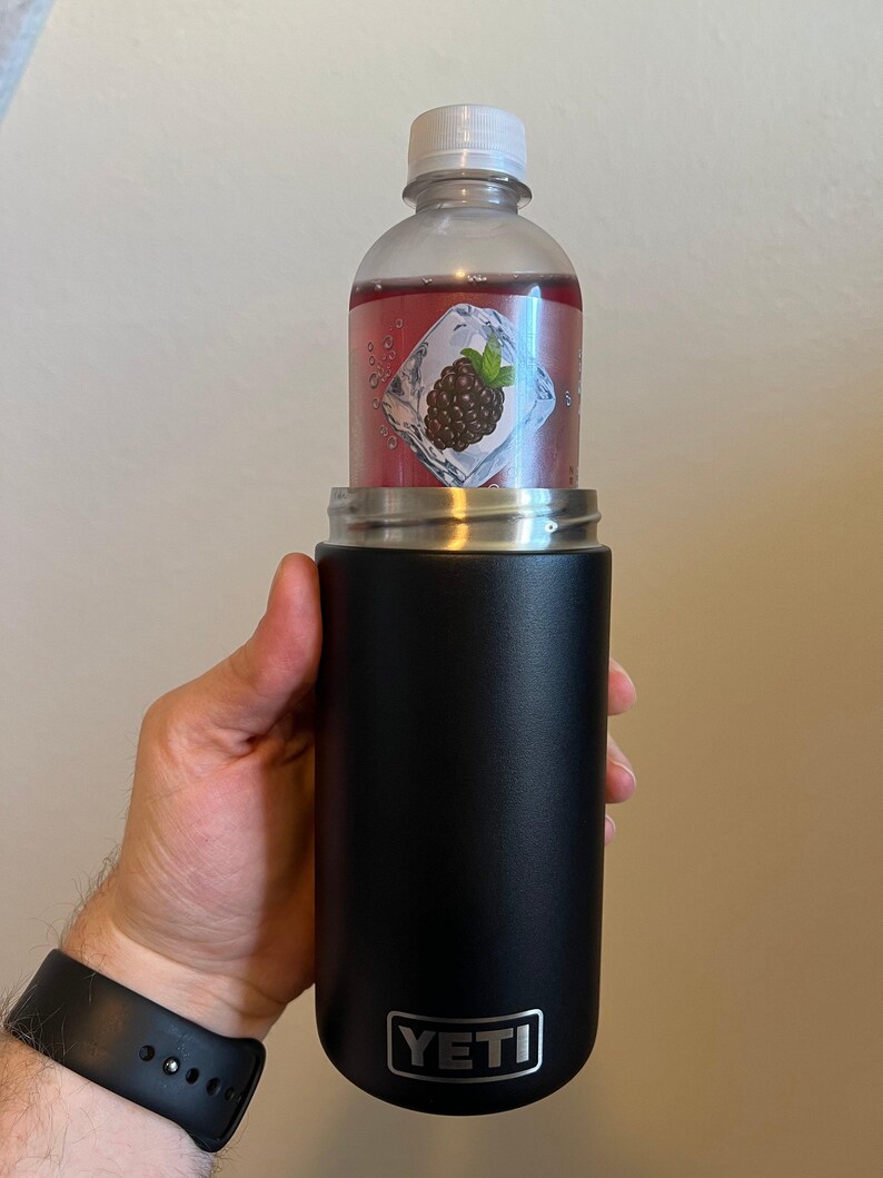 Puede incluir: Una botella YETI Rambler negra de 12 oz con una tapa negra y una botella de pl&aacute;stico transparente con un l&iacute;quido rojo en su interior. La botella de pl&aacute;stico tiene una etiqueta con un gr&aacute;fico de mora y un cubito de hielo.