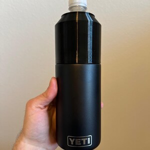 Puede incluir: Una botella aislada YETI negra con una tapa blanca. La botella est&aacute; hecha de acero inoxidable y tiene un acabado mate.