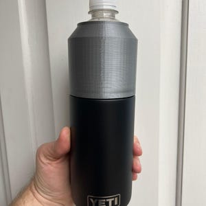 Puede incluir: Una botella de agua YETI negra con una funda de pl&aacute;stico gris. La botella est&aacute; en la mano de una persona.