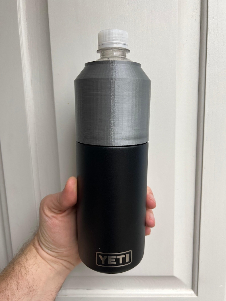 Puede incluir: Una botella de agua YETI negra con una funda de pl&aacute;stico gris. La botella est&aacute; en la mano de una persona.