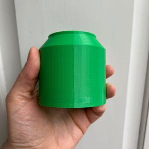 Puede incluir: Un contenedor cil&iacute;ndrico de color verde brillante impreso en 3D con una superficie lisa y ligeramente texturizada.