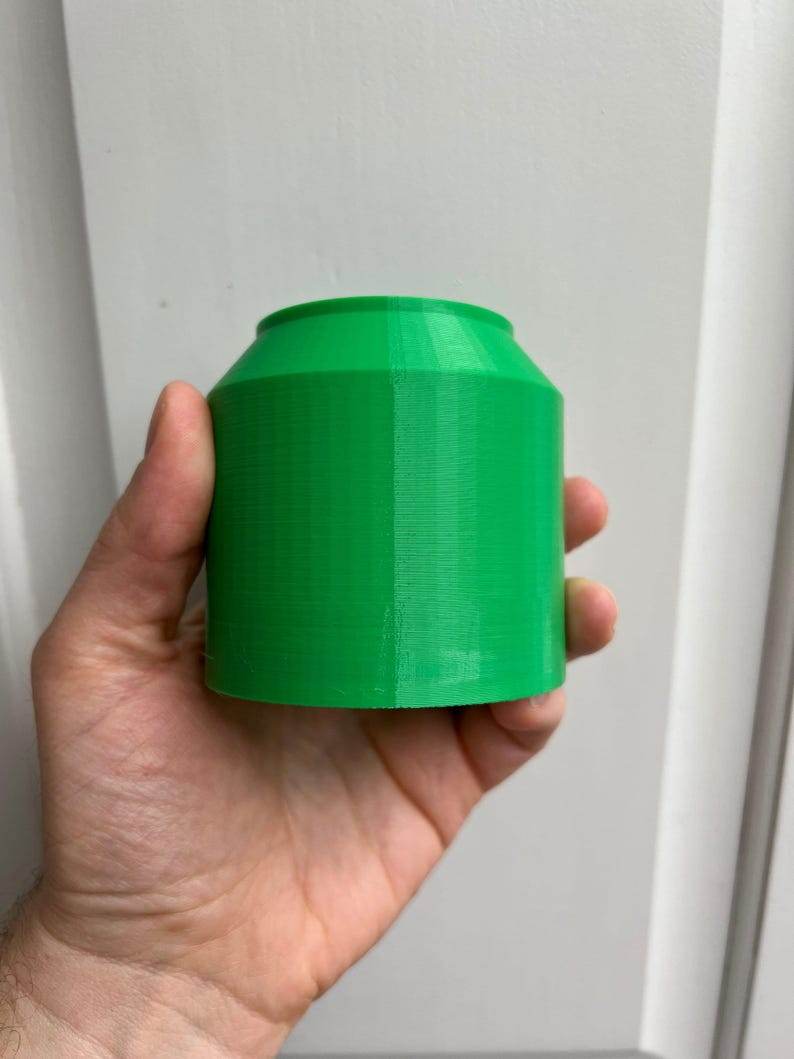 Puede incluir: Un contenedor cil&iacute;ndrico de color verde brillante impreso en 3D con una superficie lisa y ligeramente texturizada.