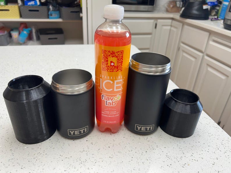 Puede incluir: Cuatro vasos t&eacute;rmicos negros de la marca Yeti, dos con tapas, y una botella de pl&aacute;stico transparente con una etiqueta roja y naranja que dice "Sparkling Ice Flavor Lab".