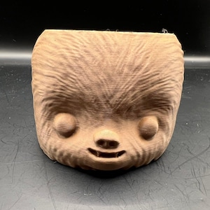 Może przedstawiać: Brązowa figurka wydrukowana w 3D przedstawiająca futrzane stworzenie z dużymi oczami i szerokim uśmiechem. Figurka została stworzona, aby przypominać postać z popularnego filmu science fiction.